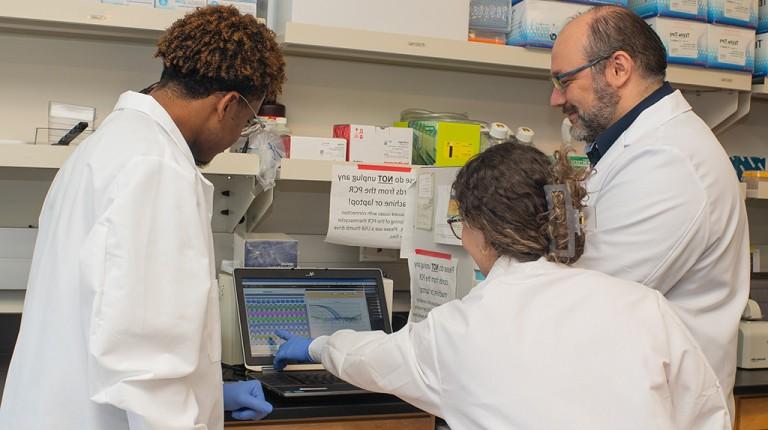 Two U N E students and a professor review research data on a computer